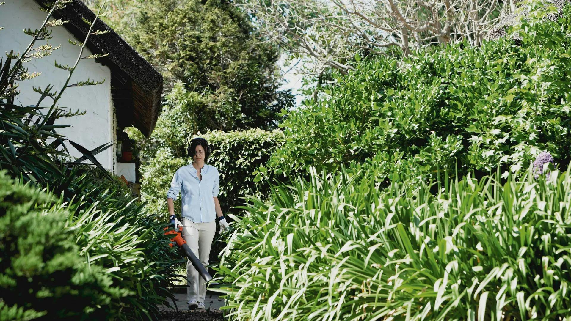 woman with leaf blower in leafy backyard